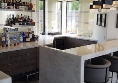 Modern home bar area with marble countertops and a well-stocked liquor shelf.
