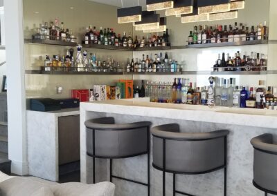 Modern bar area with stools and an assortment of beverages on shelves.