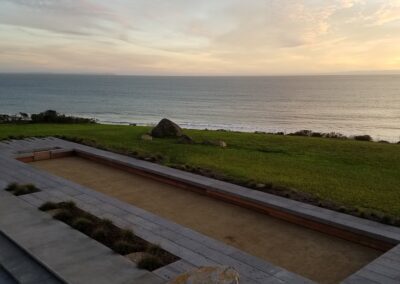 Seaside view at sunset with terraced grassy areas and benches.