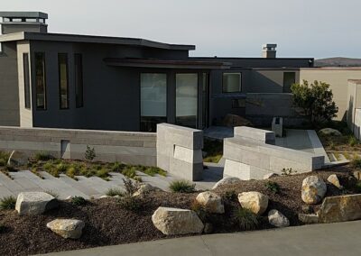 Modern single-story home with large windows, flat roof, and landscaped garden with stone details.