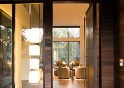 Modern home entrance with open glass door revealing a cozy interior living space at sunset.