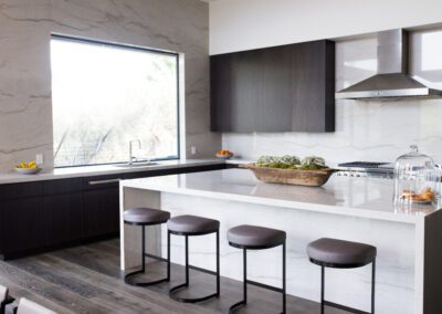 Modern kitchen with marble countertops, stainless steel appliances, and a breakfast bar with stools.