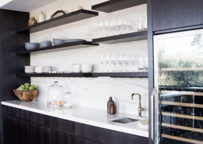 A modern kitchen with dark cabinetry, floating shelves, white countertops, and a built-in wine fridge.