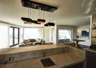 Modern kitchen with marble countertops overlooking a living room with expansive windows and water views.