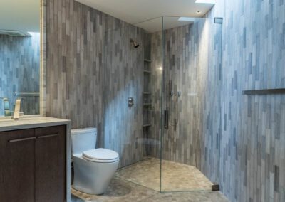Modern bathroom interior with a walk-in shower, toilet, and wood-tone vanity against a geometric tile backdrop.
