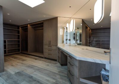 A modern walk-in closet with wooden cabinetry and an island dresser, featuring integrated lighting and a large mirror.