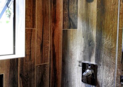 Modern bathroom with wooden tile wall featuring a window and two showerheads.