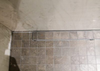 A corner view of a tiled shower floor with visible signs of mildew and soap scum buildup on tiles and glass.