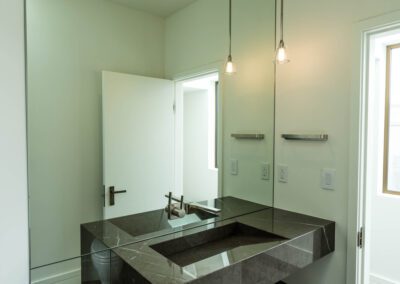 A modern bathroom featuring a dark stone sink, pendant lights, and a wall-mounted mirror.